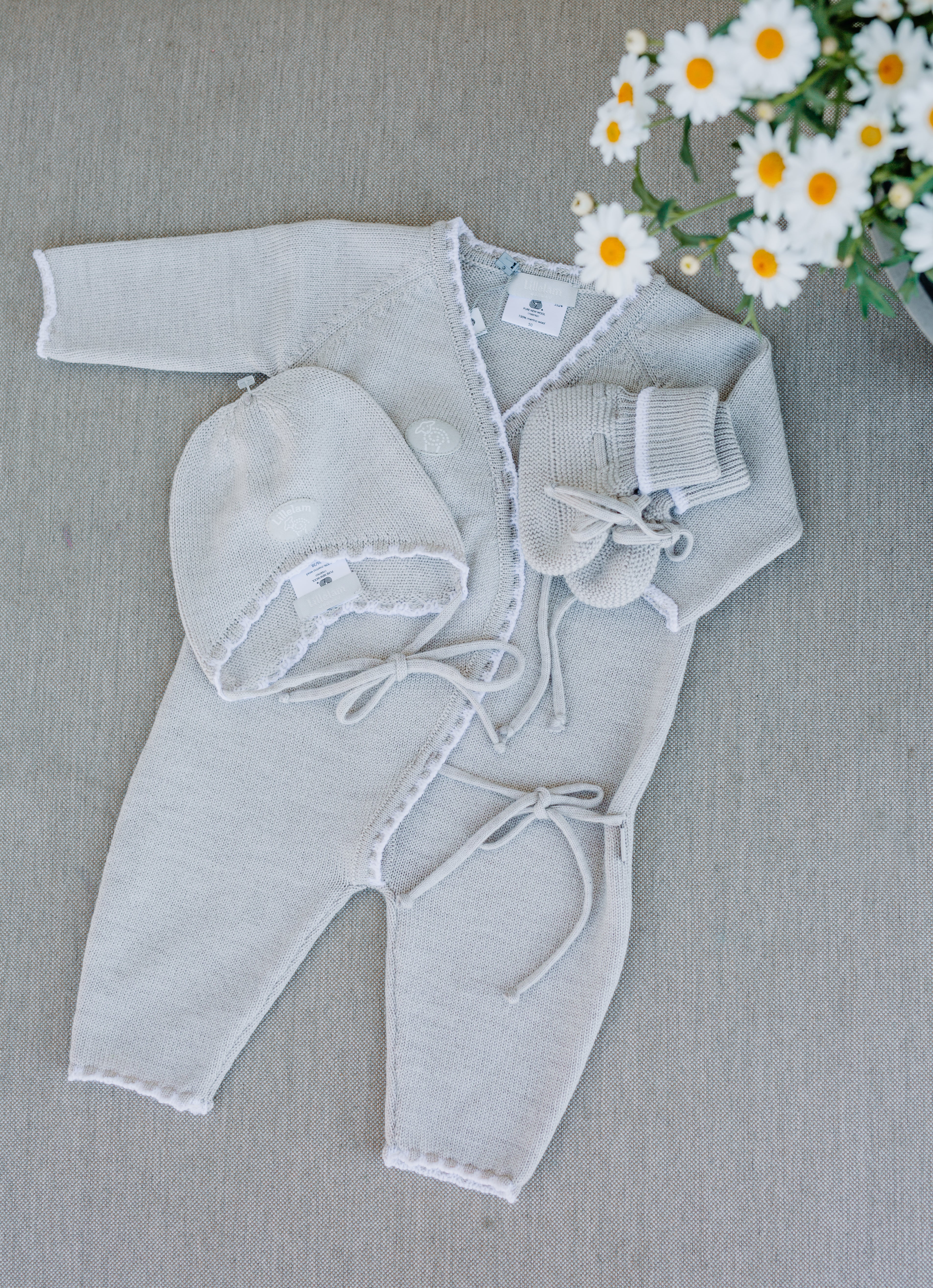 Baby outfit with cardigan, pants, and hat on a gray surface with flowers in the background