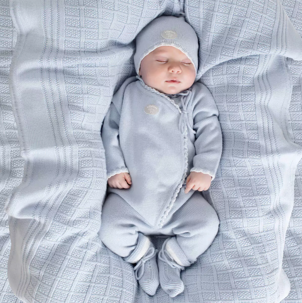 Baby in a gray outfit lying on a textured blanket