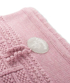 A close-up of a dusty pink knit textile, likely a baby blanket or swaddle, featuring a textured bobble pattern and a circular light gray brand patch reading 'Lil'elakm'.