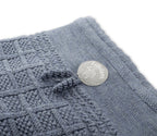 Close-up of a textured knit blanket in a dusty blue-gray color, featuring a small round white brand tag that reads 'Lil'lem' with a tree logo.