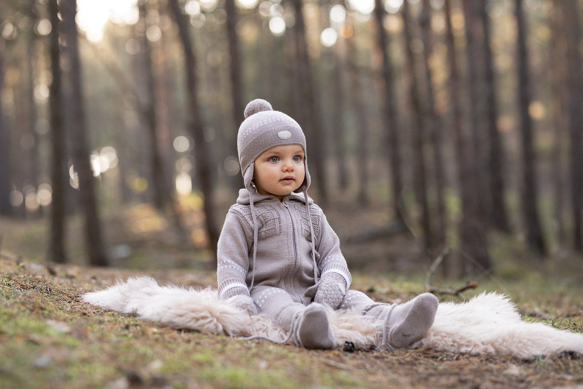 Baby in a gray outfit sitting on a white rug in a forest