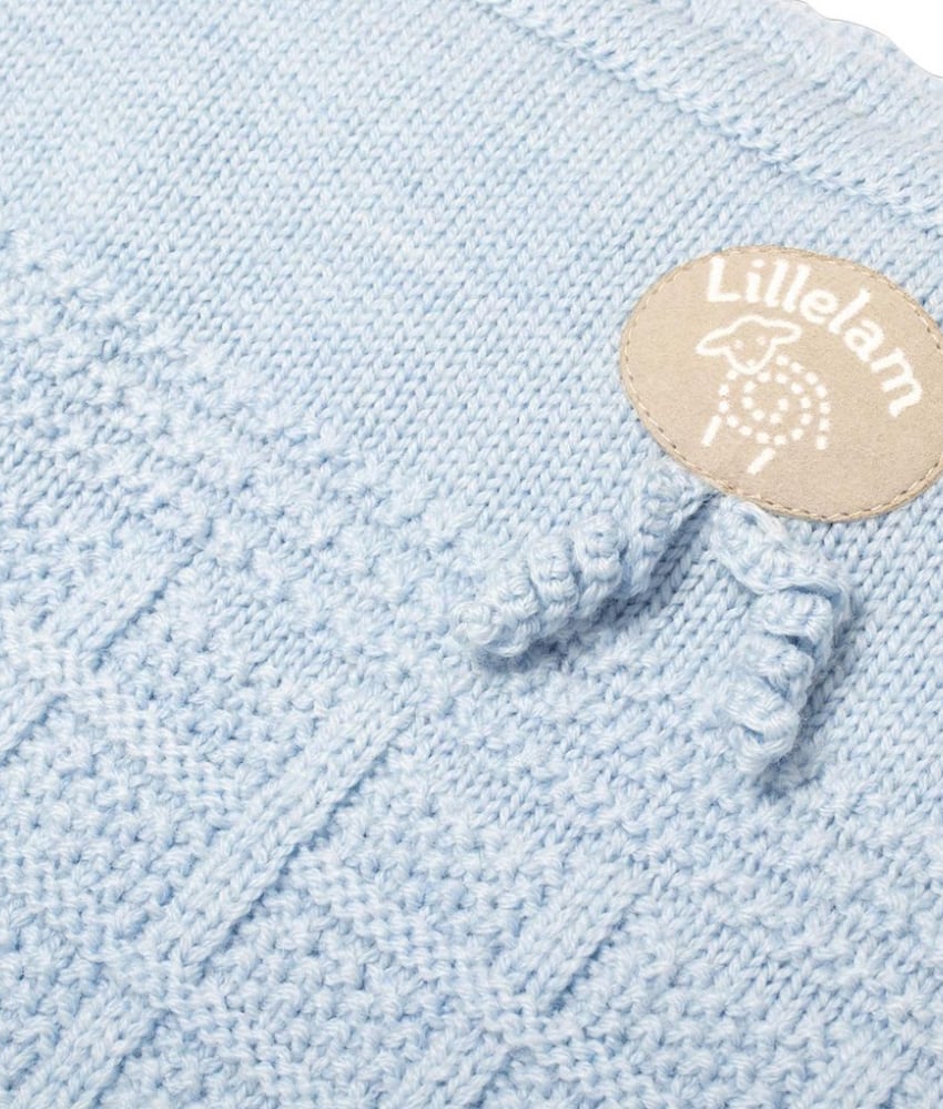 Close-up of a light blue knitted textile with a small oval beige Lilletam logo patch and knotted tassels.